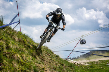 Frontansicht eines Mountainbike Downhill Rennfahrers mit Seilbahn im Hintergrund in den österreichischen Alpen