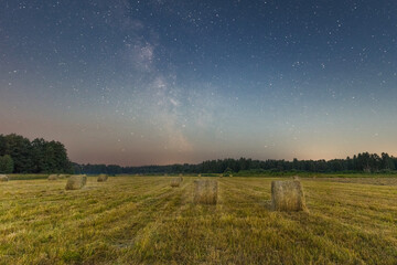 Fototapeta na wymiar Rural field with wheat sheafs after harvest in night time and sky with stars and milky way