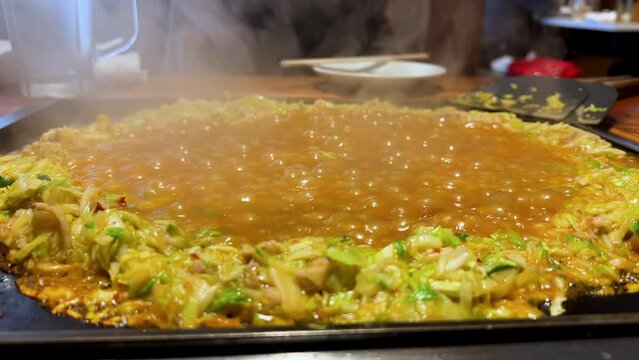 Cooking monjayaki on a hot plate. Japanese snack. A savoury soupy pancake