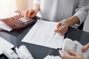 Woman accountant using a calculator and laptop computer while counting taxes for a client. Business...