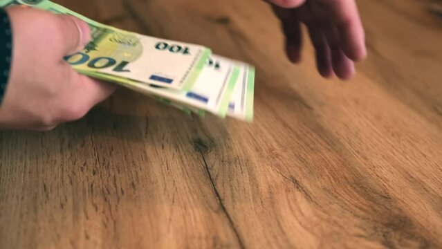 Male hands collect scattered money euro bills from wooden table by stacking them in wad, close up. Businessman takes part of profit of deal. Bribery and extortion of money concept.