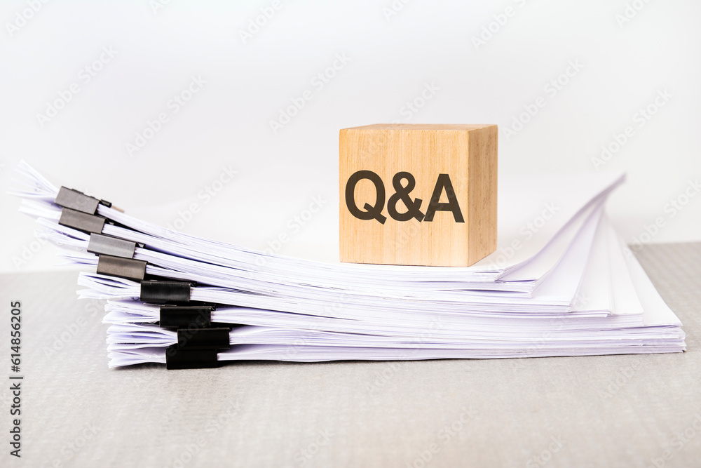 Poster a wooden cube with a text q and a on a stack of documents. grey table, white background