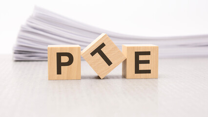 Obraz premium wooden block with text PTE - acronym - Pearson Tests of English. wooden blocks are on the paper white background, business concept. front view.