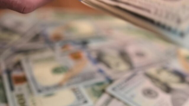 Hand gives a pack of one hundred dollar bills, another male hand takes it and throws it into a pile of money on a wooden table, close up, revolves. Bribery and extortion of money concept.