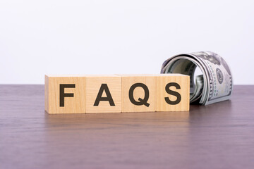 the word faqs on wood cubes and banknotes on the background, business and finance concept