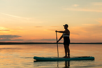 A man on a SUP board with a paddle swims in the calm water of the lake against the background of...