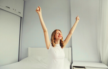 Fototapeta na wymiar Healthy sleep, happy cheerful young woman having fun or waking up on soft comfortable bed in white bedroom