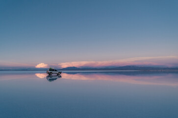 Car parked in the salt flats of Uyuni, Bolivia, with purple sky after sunset and reflection of the landscape in the water. 