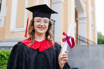 Portrait of a happy smiling graduated student girl in black mortarboard holding diploma. Celebrating graduation ceremony.
