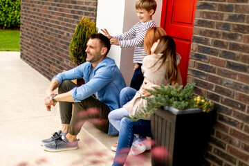 Family with a mother, father, son and daughter sitting outside on the steps of a front porch of a...