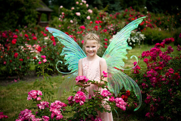 little beautiful girl in a fairy costume of butterfly having fun in roses garden on sunny summer...