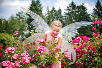 little beautiful girl in a fairy costume of butterfly having fun in roses garden on sunny summer...