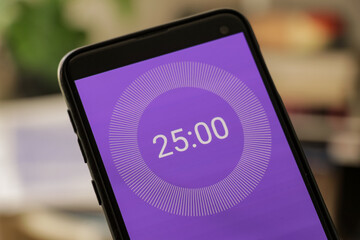 A phone with a purple and white 25-minute timer to study with the pomodoro method on a blurry...