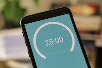 A phone with a blue and white 25-minute timer to study with the pomodoro method on a blurry background. Perfect for students planning their time studying, doing homework, being productive. - obrazy, fototapety, plakaty
