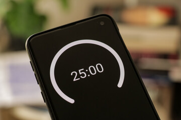 A phone with a black and white 25-minute timer to study with the pomodoro method on a blurry background. Perfect for students planning their time studying, doing homework, being productive.