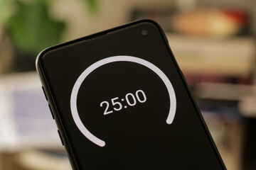 A phone with a black and white 25-minute timer to study with the pomodoro method on a blurry background. Perfect for students planning their time studying, doing homework, being productive. - obrazy, fototapety, plakaty