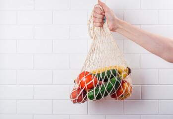 Woman's hand holding mesh string bag full of fruits and vegetables. International plastic free day...