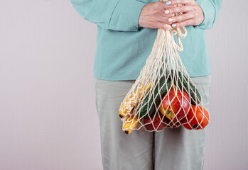 Woman holding mesh string bag full of fruits and vegetables. International plastic free day background, shopping concept. 3rd of July. Copy space