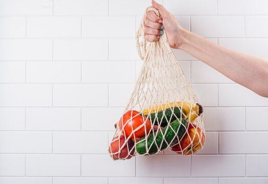 Woman's hand holding mesh string bag full of fruits and vegetables. International plastic free day background, shopping concept. 3rd of July. Copy space - Powered by Adobe
