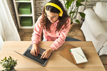A young woman, focused and productive, working at her home desk with a laptop, enjoying music...