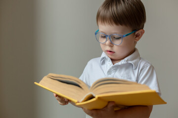 smart kid holds a thick book in his hands, the boy wears glasses