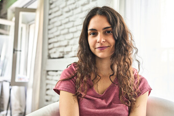 A young Caucasian woman, sitting in a cozy armchair in her home, happily enjoying the morning with contentment.