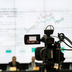 Camera during press conference with speaker in the background