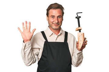 A middle-aged shoe maker smiling cheerful showing number five with fingers.