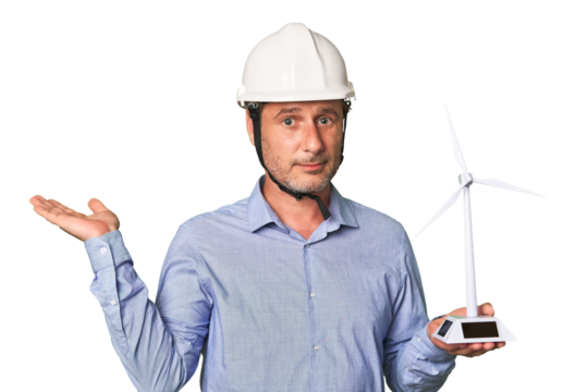 A middle-aged architect man holding a windmill model showing a copy space on a palm and holding another hand on waist.