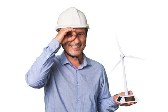 A middle-aged architect man holding a windmill model excited keeping ok gesture on eye.