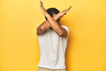 Casual young Latino man against a vibrant yellow studio background, keeping two arms crossed,...