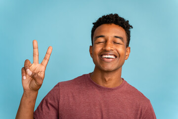 Smiling young man making peace sign with fingers.