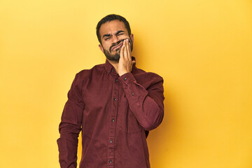 Casual young Latino man against a vibrant yellow studio background, having a strong teeth pain, molar ache.