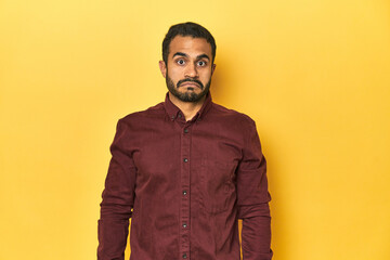 Casual young Latino man against a vibrant yellow studio background, sad, serious face, feeling miserable and displeased.