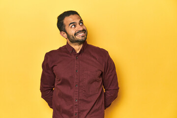 Fototapeta premium Casual young Latino man against a vibrant yellow studio background, relaxed and happy laughing, neck stretched showing teeth.