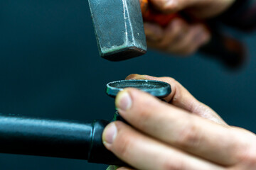 A bicycle mechanic holds a hammer in his hand on a black background. An old black highway in a...