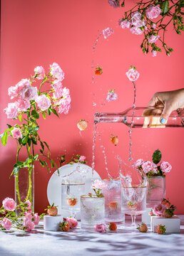 Different elegant glasses with sparkling wine, pink roses and strawberry, women hand is pouring wine from bottle to glass