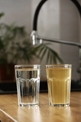 House water filtration system to drinkable condition. Glass of clear water after reverse osmos filtration and glass of dirty water on tabletop on kitchen. Evidence of contamination of tap water