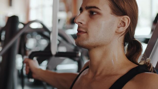 Close-up portrait of a athletic fitness man doing exercises on a peck deck working out in gym. Muscular body builder doing chest on the machine