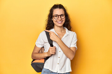 Caucasian university student with glasses, backpack, smiling and pointing aside, showing something...