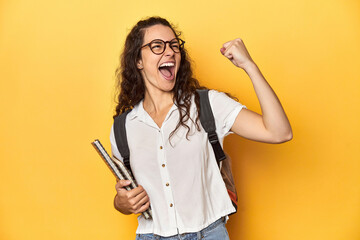 Student holding notebooks, glasses, backpack on, raising fist after a victory, winner concept.