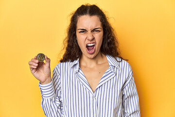 Woman holding a physical Bitcoin coin, screaming very angry and aggressive.