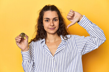 Woman holding a physical Bitcoin coin, showing a dislike gesture, thumbs down. Disagreement concept.
