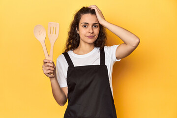 Woman with apron, wooden cooking utensils, yellow, being shocked, she has remembered important...