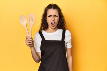 Woman with apron, wooden cooking utensils, yellow, screaming very angry and aggressive.