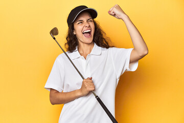 Golfer woman with cap, golf polo, yellow studio, raising fist after a victory, winner concept.