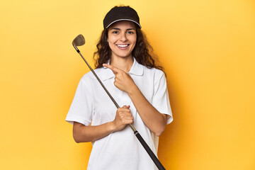 Golfer woman with cap, golf polo, yellow studio, smiling and pointing aside, showing something at blank space.