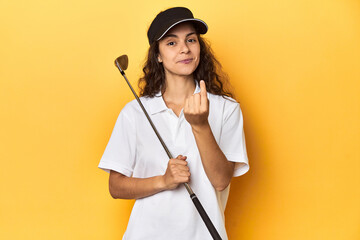 Golfer woman with cap, golf polo, yellow studio, pointing with finger at you as if inviting come closer.