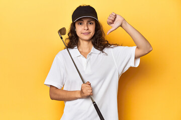 Golfer woman with cap, golf polo, yellow studio, showing a dislike gesture, thumbs down. Disagreement concept.