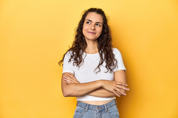 Young Caucasian woman, yellow studio background, smiling confident with crossed arms.